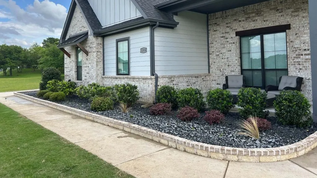 Landscape installation with black rock, shrubs and a stone-bordered bed at a new home