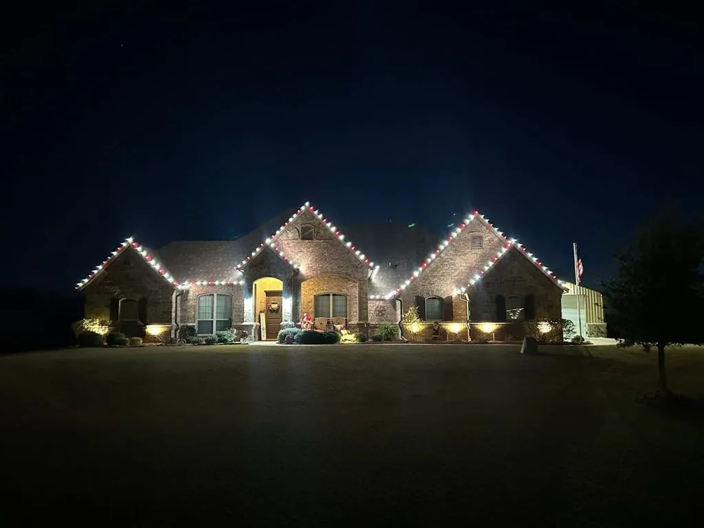 Brick home in Burleson with Christmas lights on three roof peaks and landscape lighting
