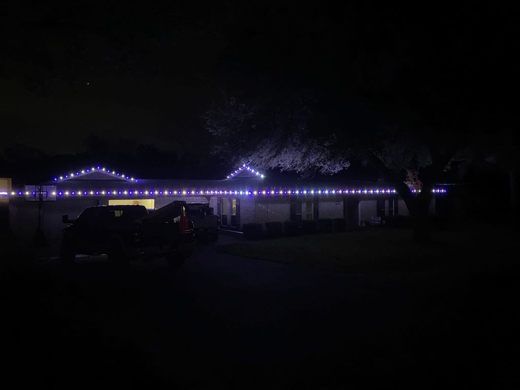 Long ranch home outlined in purple holiday lights at night