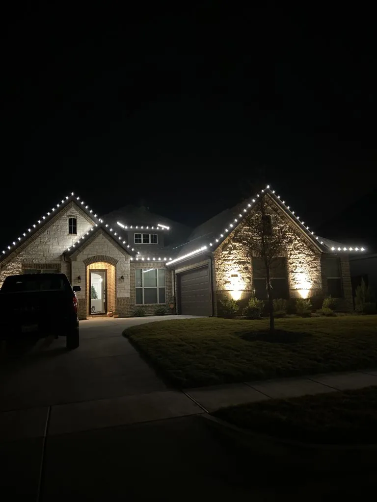 Stone home in Burleson, TX with white Christmas lights outlining every roof peak, installed by Maverick Lawn & Landscaping