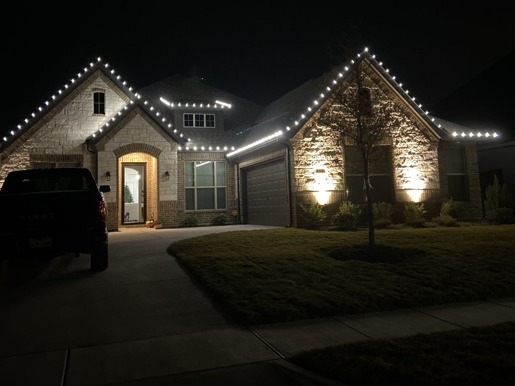 Stone home in Burleson, TX with holiday lights on the rooflines and lit landscaping